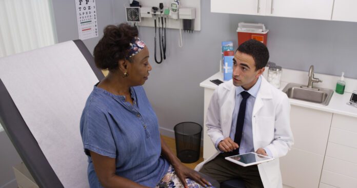 Older black woman explaining health issue to young male hispanic doctor in office