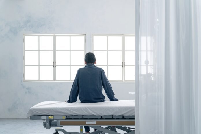 Depressed inpatient sitting on bed in hospital room.